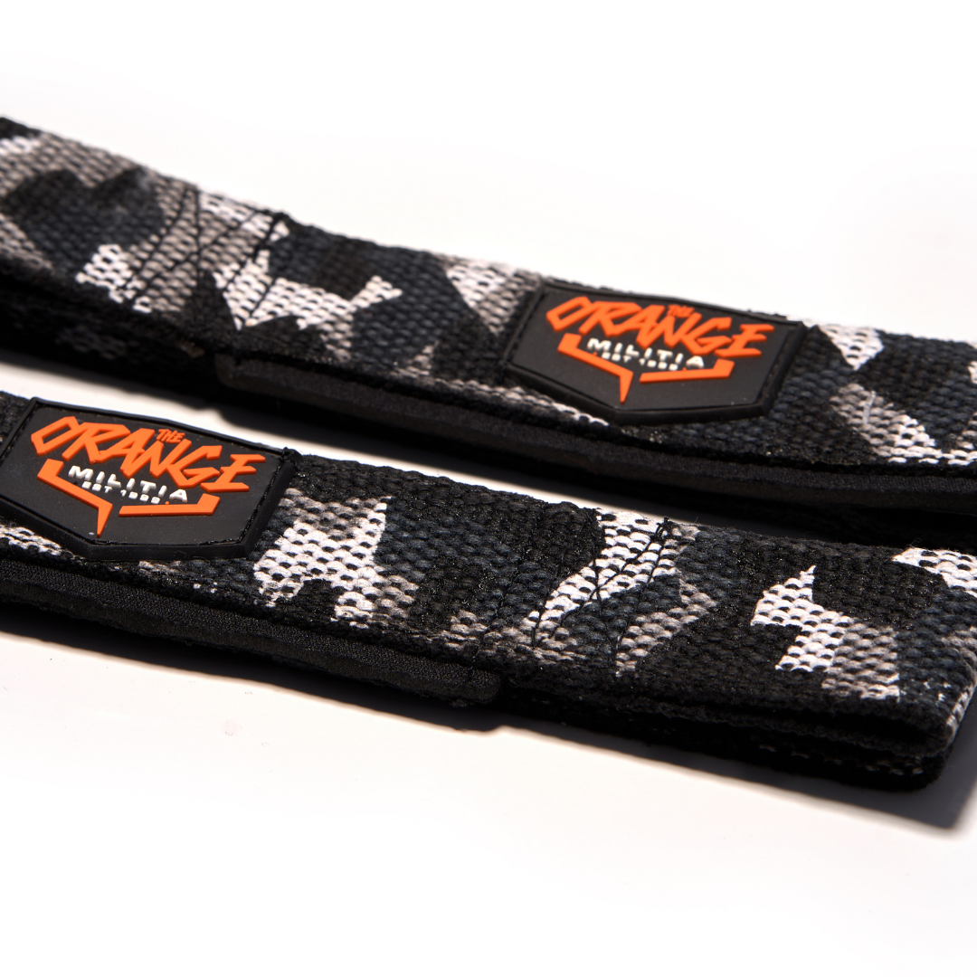 A pair of black and white camouflage patterned lifting straps with the 'ORANGE MILITIA' brand logo on the buckle.